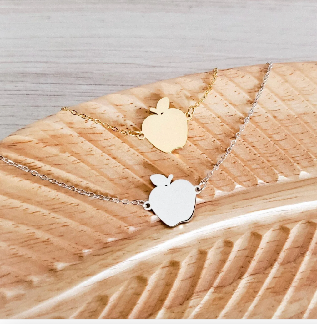 Two apple-shaped pendants on gold and silver chains against a wooden background