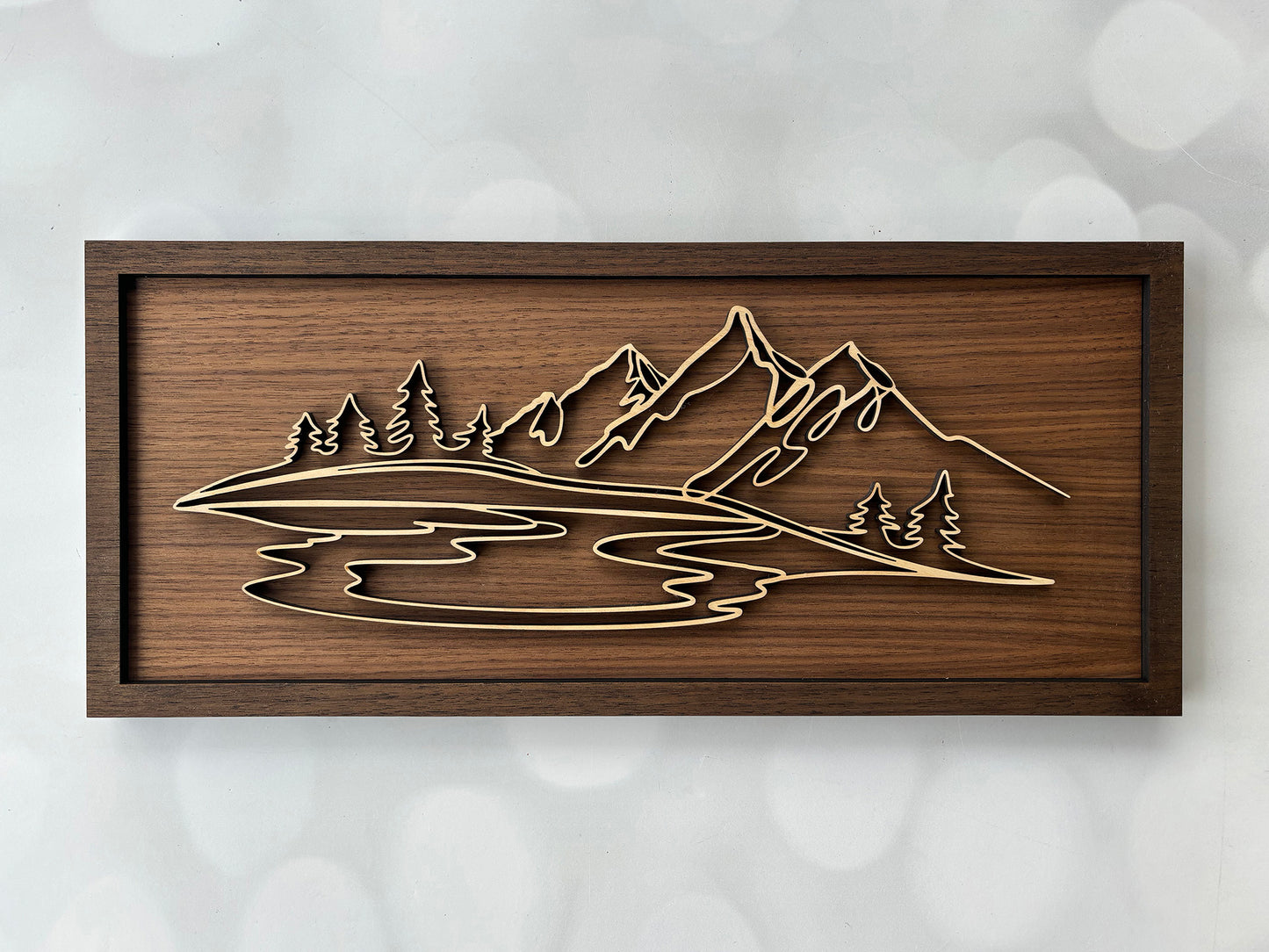 Wooden wall art with mountain and lake design on a textured white background