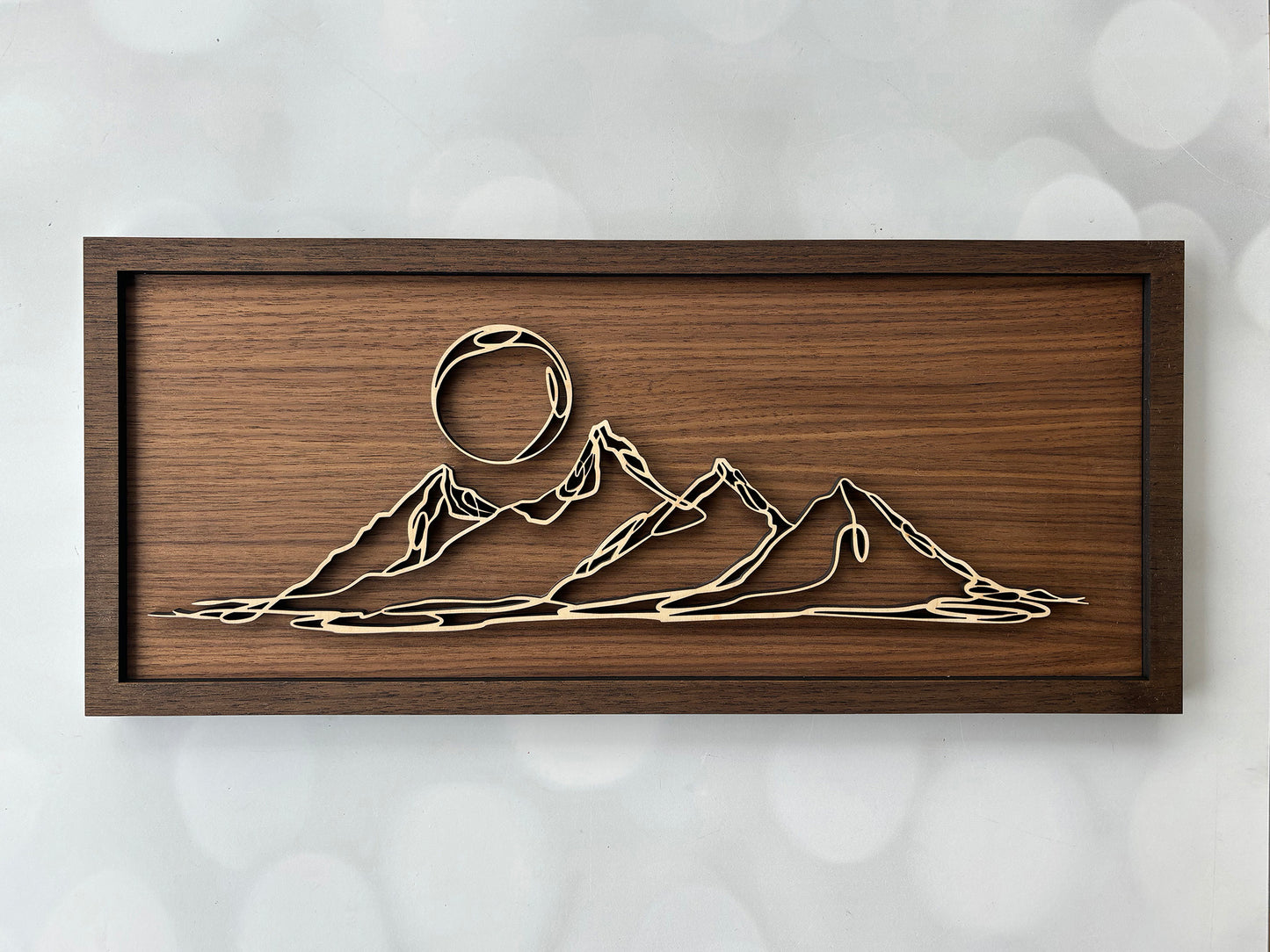 Wooden wall art with mountain and sun design on a textured white background