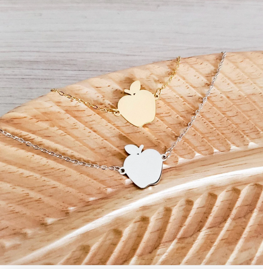 Two apple-shaped pendants on gold and silver chains against a wooden background