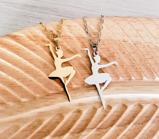 Two ballerina pendants on necklaces on a wooden surface