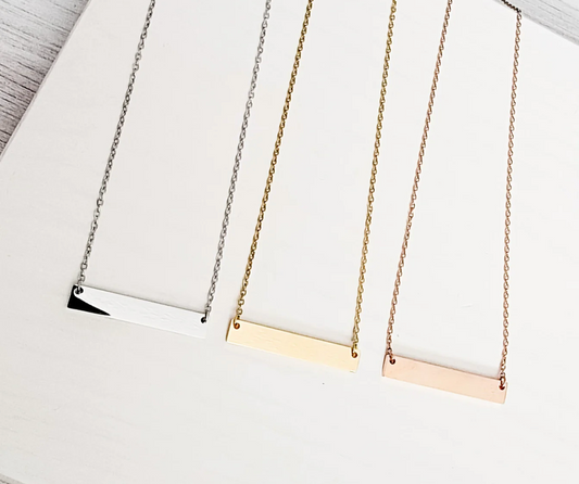 Three necklaces with horizontal bar pendants in silver, gold, and rose gold on a white surface.