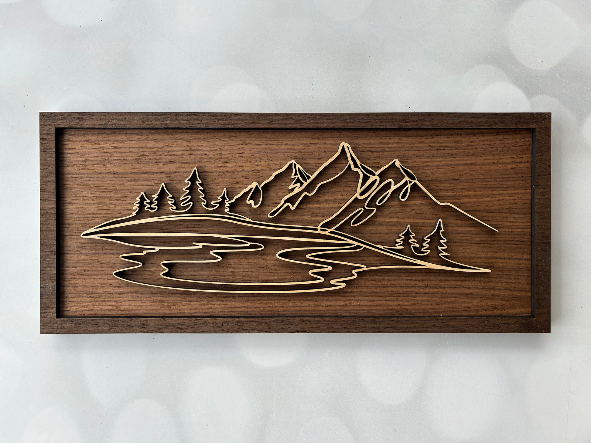 Wooden wall art with mountain and lake design on a textured white background